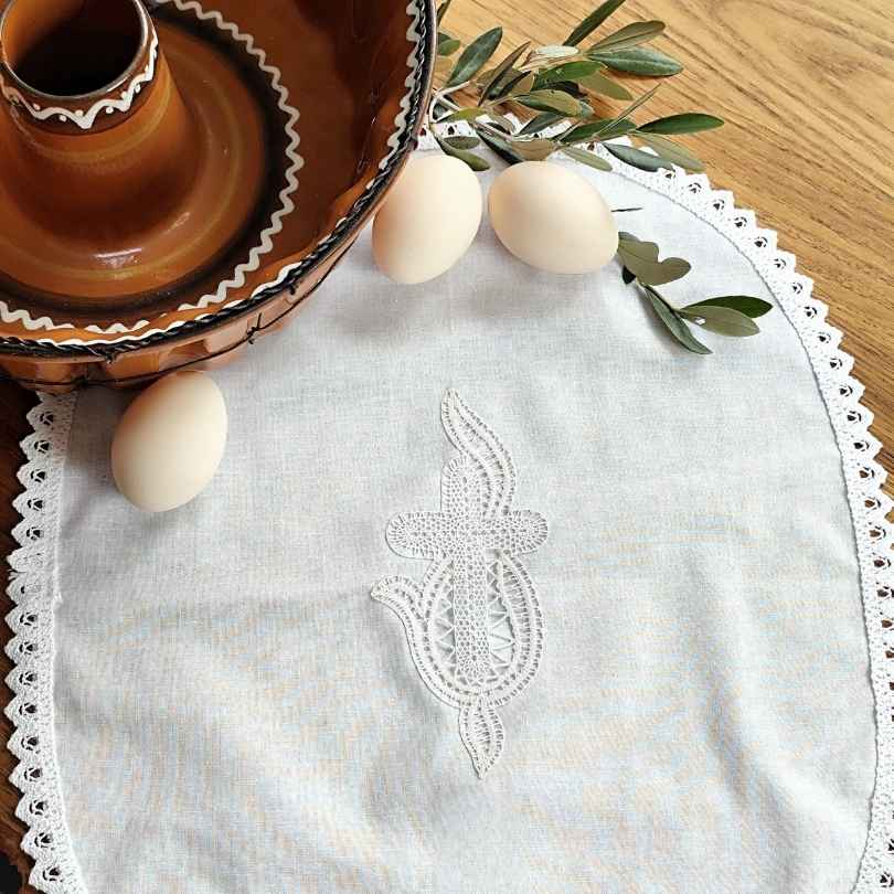 Ročno izdelan velikonočni prtiček z nežno klekljano čipko. Ovalna oblika in klekljan motiv križa s plameni. Možna izdelava v velikosti po naročilu.